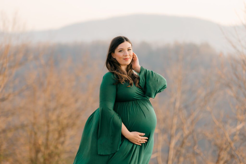 Expecting mother at 36 weeks, standing on a scenic overlook with a full belly, wearing a fitted gown and embracing her pregnancy journey