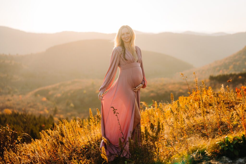 Pregnant woman in flowy pink dress on a mountain at sunset