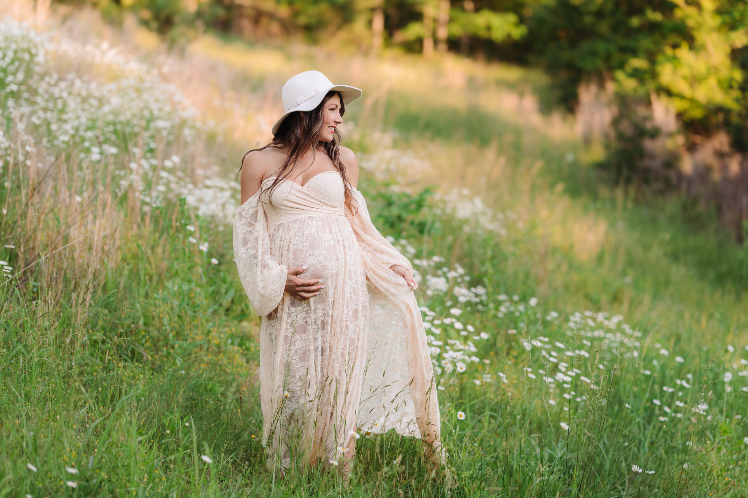 pregnant woman in beige maxi dress standing in a field of daisies Asheville maternity session