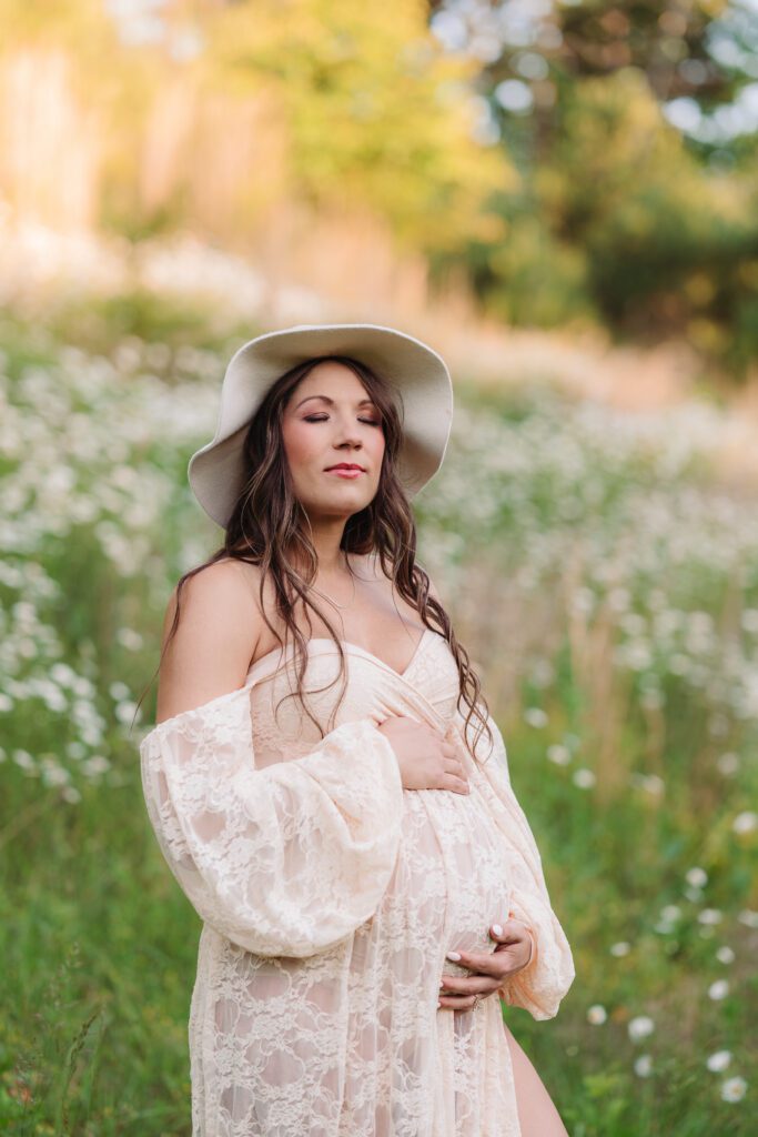 woman in flowing beige dress holding belly in daisy field maternity photos Asheville
