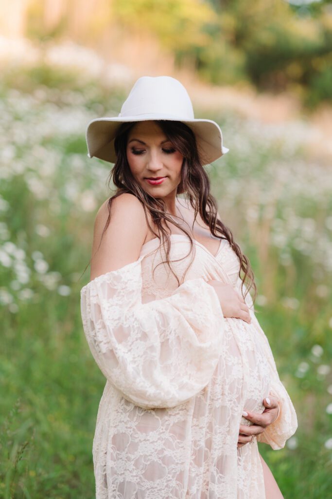 Pregnant woman wearing a hat in a field of flowers for her maternity photo session